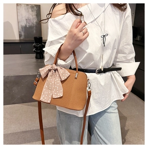 Détail d'un sac bandoulière marron texturé avec foulard en soie à pois roses et bijoux argent