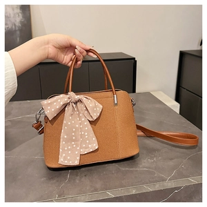 Détail du sac à main marron tissé avec un nœud en foulard à pois et une poignée