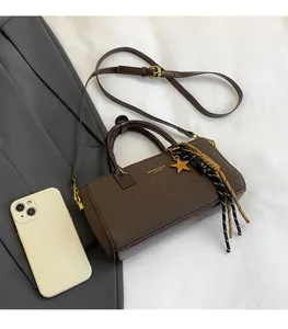 Sac à main mat marron foncé avec breloque étoile et gland à côté d'un smartphone