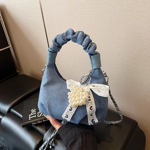 Denim blue handbag with pleated handle, lace bow, and pearl heart detail in hand