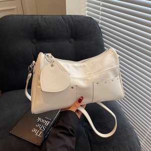 Borsa a spalla bianca lucida con borchie argentate e ciondolo a cuore su divano