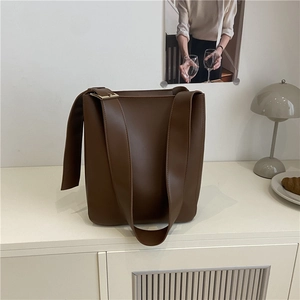Minimalist large brown leather tote bag with gold hardware on white surface