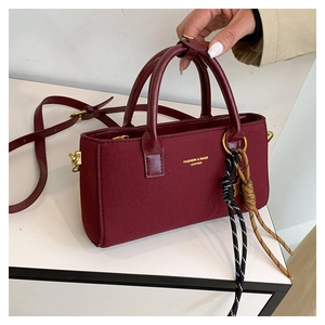 Détail d'un sac à main rouge foncé en cuir givré avec logo doré et pendentif tissé rayé