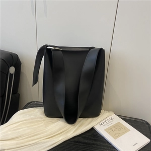 Minimalist black leather tote bag with wide shoulder strap on an artistic studio background