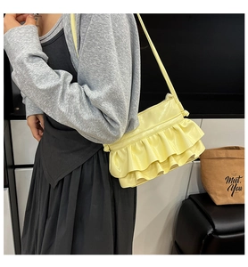 Close-up of pale yellow bucket bag with tiered ruffles and glossy finish on model