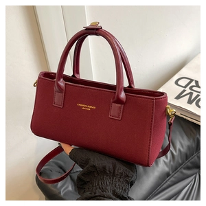 Détail du sac boston bordeaux mat avec logo doré et poignée supérieure en cuir