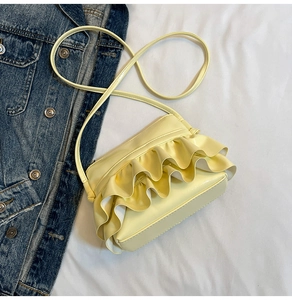 Detailed close-up of cream pleated bucket bag with ruffles on a denim jacket background