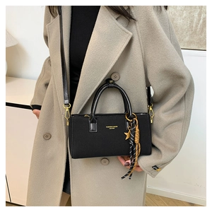 Détail du sac à main en cuir noir avec logo doré et pendentif sur un manteau