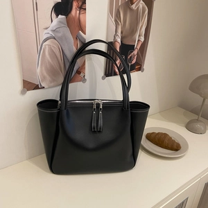 Elegant black leather trapeze tote bag with white contrast stitching on a cream desk
