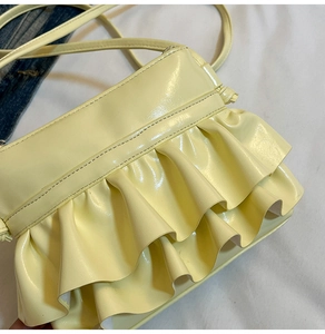 Detail of light yellow bucket bag with glossy pleated ruffles and slender leather strap