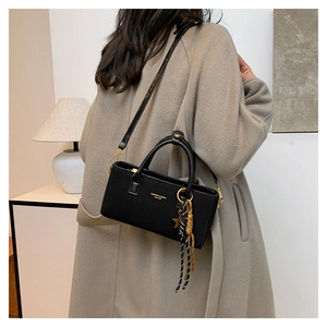 Détail d'un sac à main carré noir mat avec lettrage doré et accessoire pendentif étoile