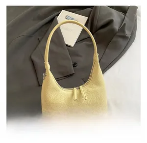 Detail view of cream leather crescent bag with dual zippers against grey blazer