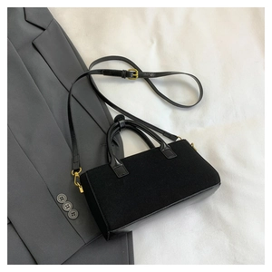 Détail d'un sac à main en feutre noir avec boucle dorée sur une veste de costume grise