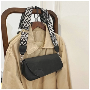 Détail d'un sac bandoulière noir avec large sangle géométrique sur un trench-coat kaki