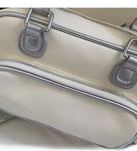 Detail view of cream-colored handbag with silver piping and dual zipper texture