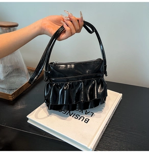 Detail of a black glossy patent leather bucket bag with elegant double ruffles on the bottom