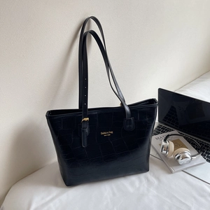 Schwarze Tote Bag aus Kunstleder mit Krokoprägung und goldenem Logo auf hellem Grund