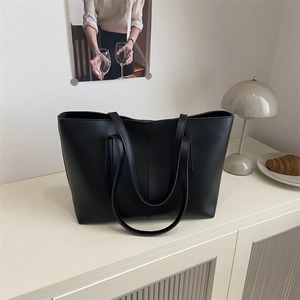 Minimalist black oversized tote bag with long straps for women in a chic indoor setting