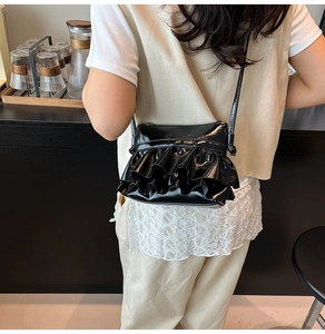 Detail of black glossy bucket bag with layered ruffle pleats worn as a crossbody bag