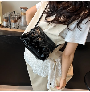 Detail shot of a black pleated crossbody bag with glossy finish and wavy textures