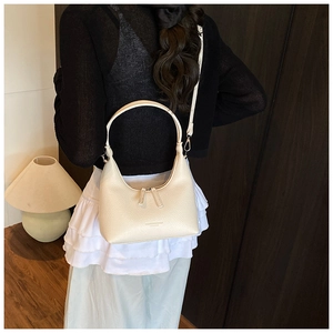 Close-up of off-white litchi grain leather shoulder bag worn by model in cozy interior