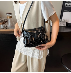 Detail of a black pleated ruffled crossbody bag in glossy patent leather finish