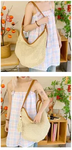 Detail of hollow-out straw hobo bag with brown leather strap and tassel accents