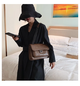 Sac bandoulière matelassé marron avec fermoir argenté porté par un mannequin dans une chambre
