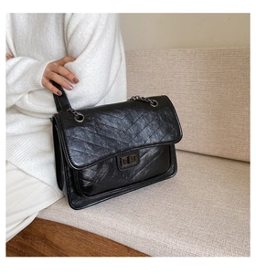 Détail de la texture en cuir verni noir avec surpiqûres en chevrons et fermoir métallique carré