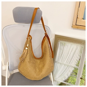 Detail of large woven straw shoulder bag with brown leather strap and tassel charm decor