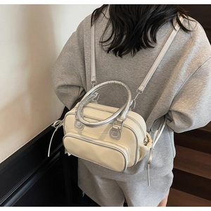 Detail of a minimalist cream-colored shoulder bag with silver metal handle and side drawstrings