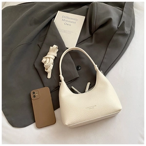 Detail view of cream hobo bag on a grey blazer showing capacity with phone case accessory