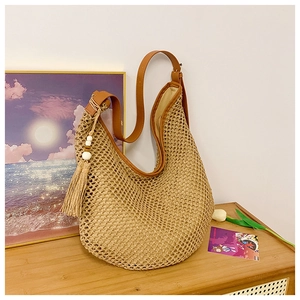 Detail of hobo straw beach bag featuring brown leather strap and tassel with wooden beads