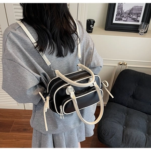Detail of a black Boston shoulder bag with white piping and dual zip pockets shown in use