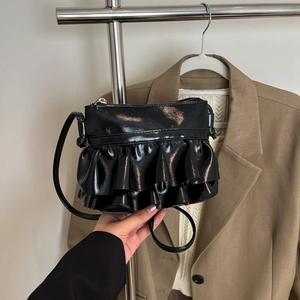 Glossy black patent leather bucket bag with pleated ruffles on a hanger display