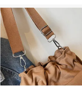 Detail of silver hardware and wide fabric strap on a brown canvas crossbody bag