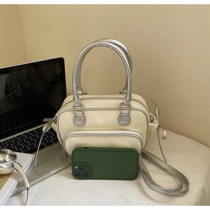 Detail of off-white crossbody bag with silver cylindrical handles and side bow knots