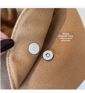 Close-up of secure silver magnetic buckles on a premium brown canvas shoulder bag