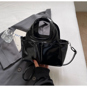 Close-up of black glossy patent leather bag with silver buckles and handle details