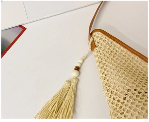 Close-up of hollow straw bag with brown leather trim and bohemian tassel details