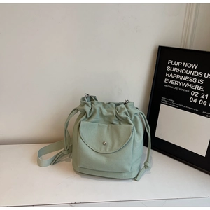 Detail of mint green canvas bucket bag with drawstring closure and metal buckle front pocket