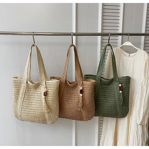 Detail of hand-woven straw tote bags in beige, brown, and green with tassel ornaments