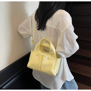 Detail of glossy light yellow crossbody bag with double front pockets on female model