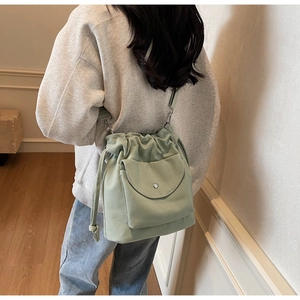 Back view of model wearing a light green canvas drawstring crossbody bag with front pocket