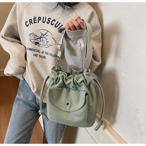 Detail of mint green canvas bucket bag featuring drawstring closure and front flap pocket
