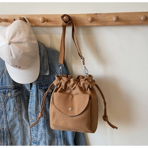 Detail of warm brown canvas bucket bag with drawstring closure and metal buckle strap