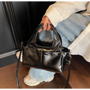 Close-up of glossy black handbag with dual front pockets and adjustable strap detailing