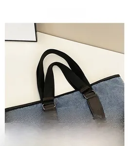 Detail of blue denim tote bag showing black webbing handle and brown leather reinforcement