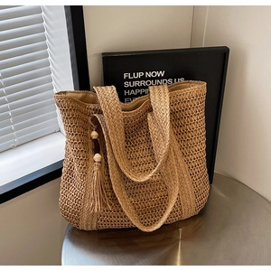 Detail of straw woven tote bag texture with wide shoulder straps and tassel charm detail