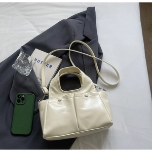 Detail shot of a minimalist cream shoulder bag with double front pockets on a grey suit